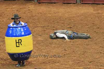 A rodeo clown/barrel man watches a bull while he waits by a fallen bull rider