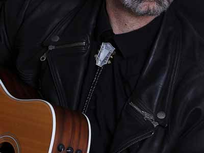 A musician wearing a bolo tie shaped like the headstock of a guitar