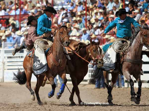 A saddle bronc rider gets off with help from the pickup men