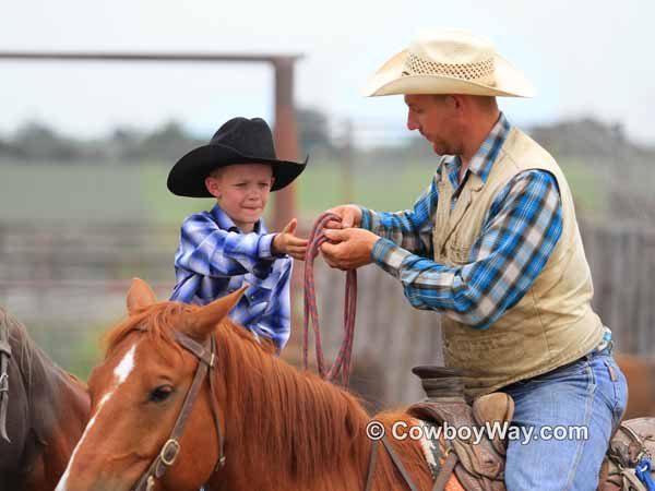 A little cowboy on his horse takes a rope from an older cowboy