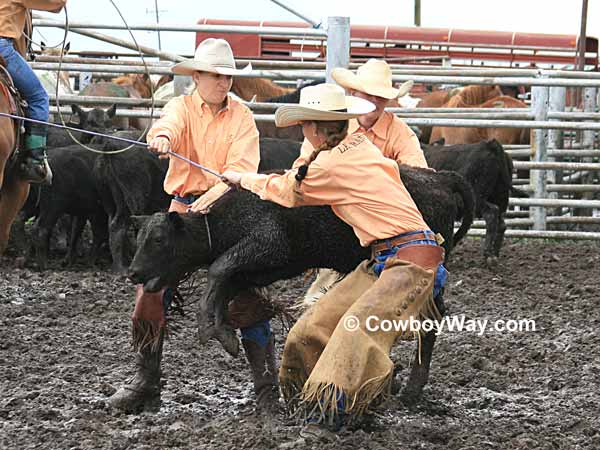 Three cowgirls try to mug a calf in the mud