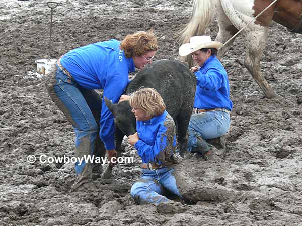 Three cowgirls in deep mud with a calf