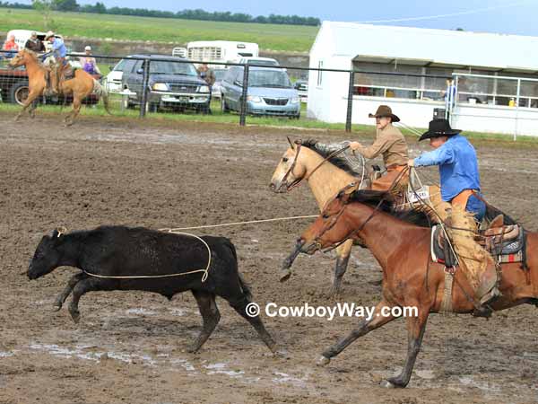 A cowboy ropes a steer in a muddy arena