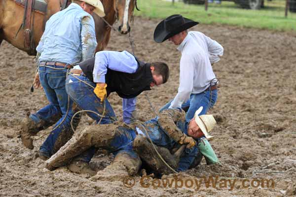 A cowboy covered in mug holds a steer down at a ranch rodeo
