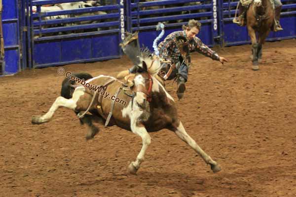 A bronc rider makes a flying dismount off of a saddle bronc