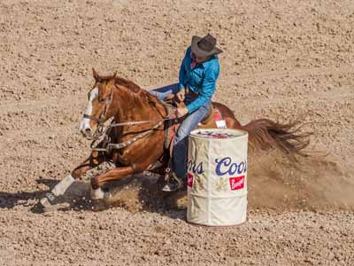 A barrel racer sits deep in her saddle as she takes a hard, fast turn around a barrel